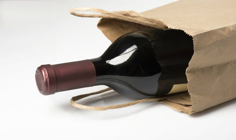 A bottle of red wine in a paper bag, perhaps being given as a gift or bought at a liquor store, on a white background with reflection and shadow