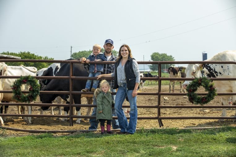 farming family standing in front of fence and cows