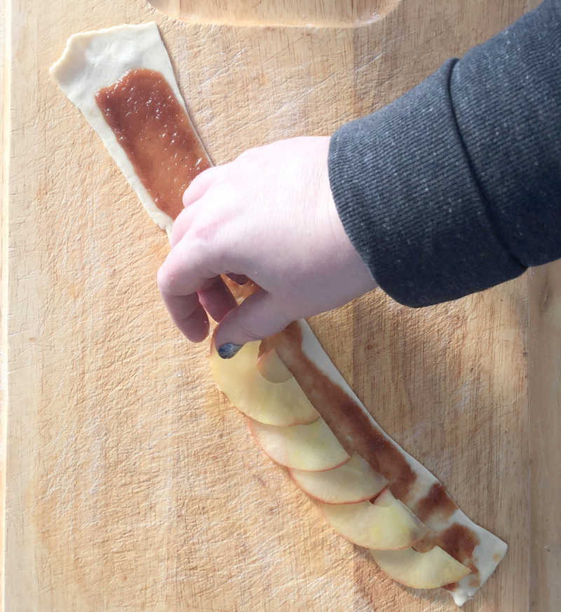 hand placing apple slices on pastry strip