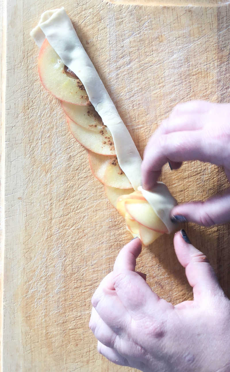 hand rolling pastry strip with apples
