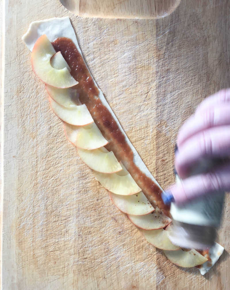 hand sprinkling cinnamon on apple slices on pastry