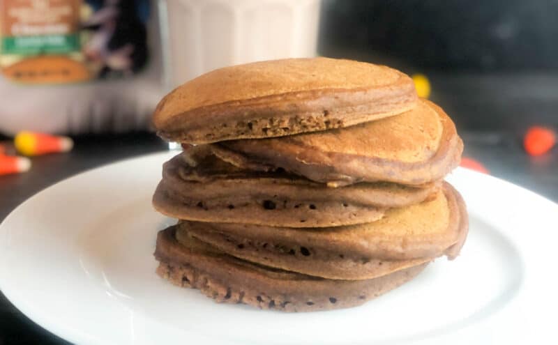stack of chocolate pumpkin pancakes with syrup and whipped cream