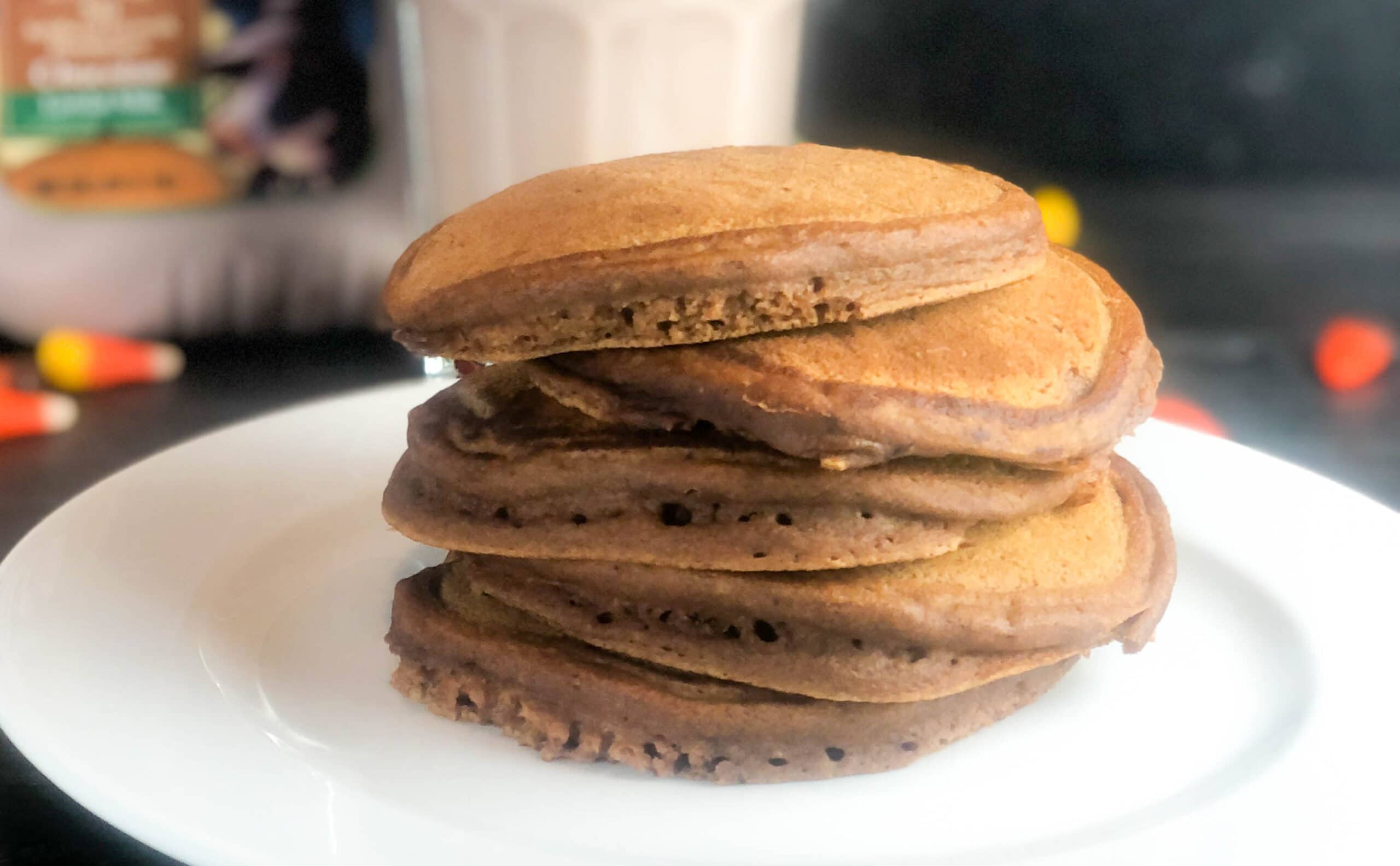 stack of chocolate pumpkin pancakes with syrup and whipped cream