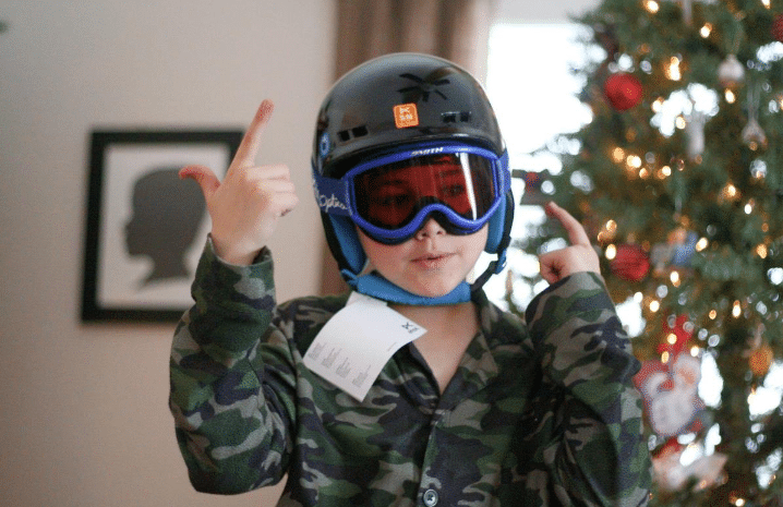 child with snowboard helmet on in front of xmas tree