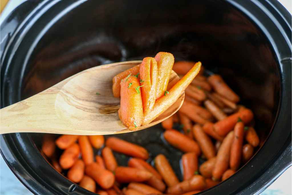 tender crock pot baby carrots on a wooden spoon