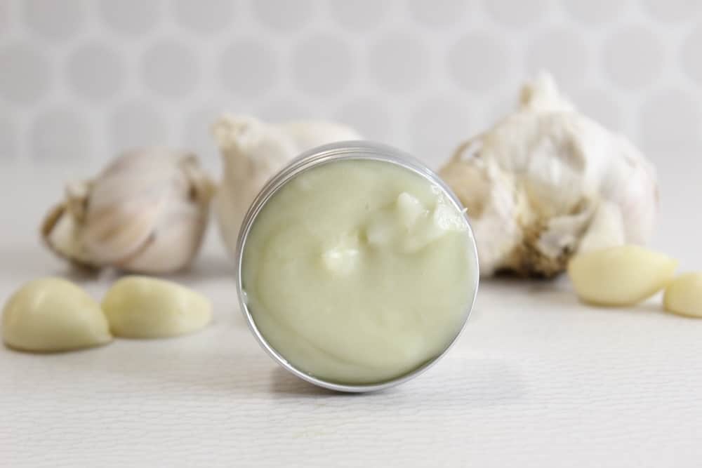 a tin of garlic salve with garlic cloves behind it