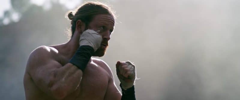 Shirtless man in fighting stance with wrapped hands