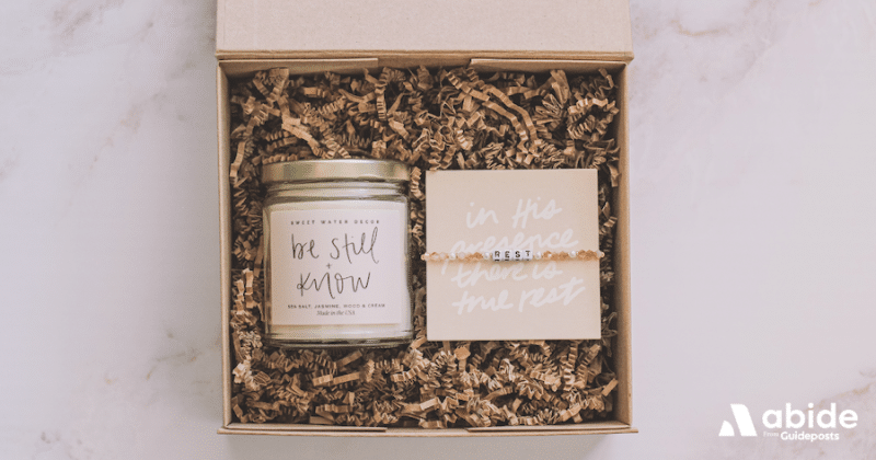 A jar candle with be still and know on the label next to  bracelet with the word rest.