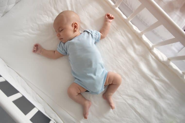 Baby in a blue onesie laying on his back in a crib.